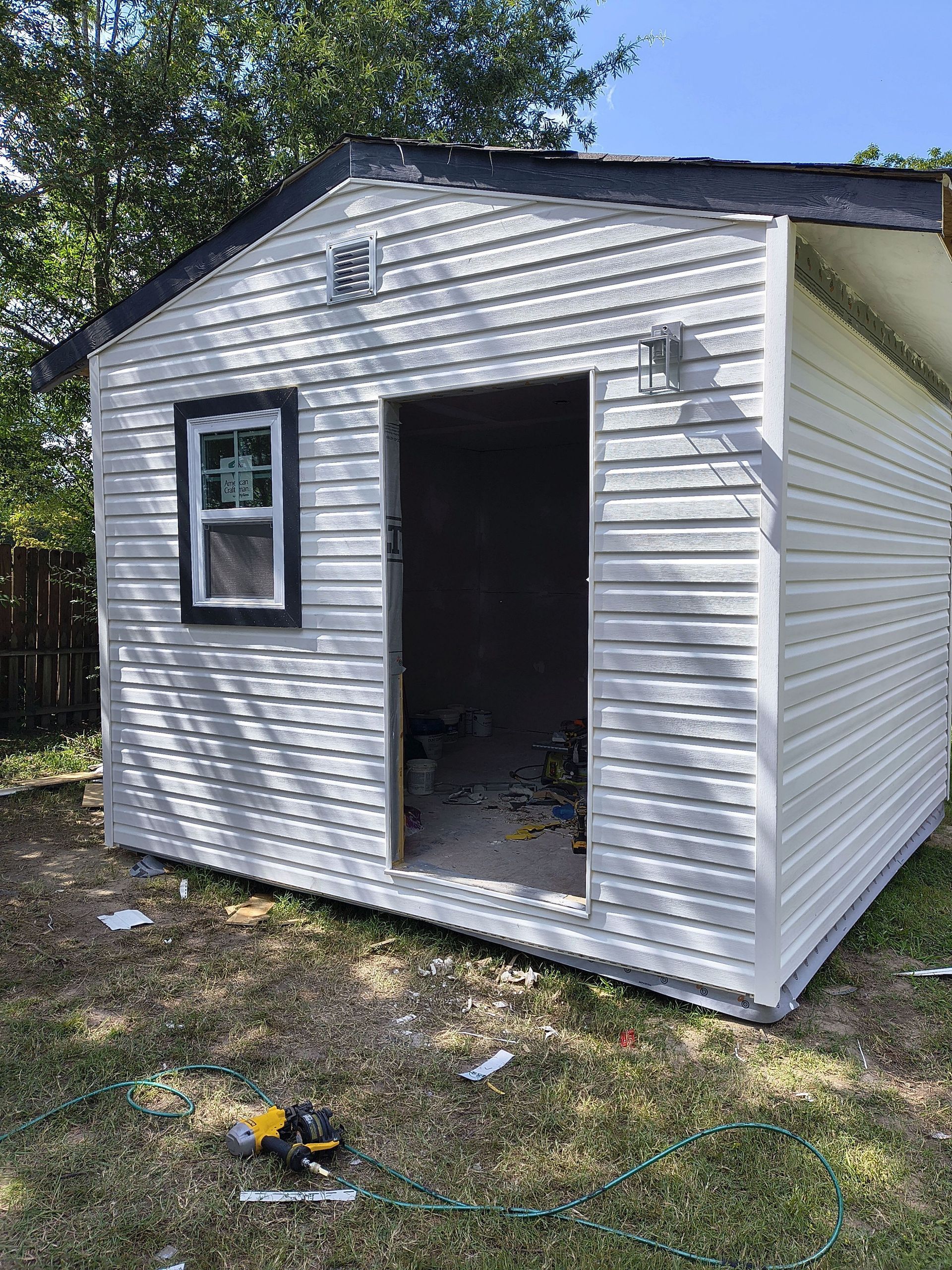 Small white shed with an open doorway and a window, set outdoors on a grassy yard.
