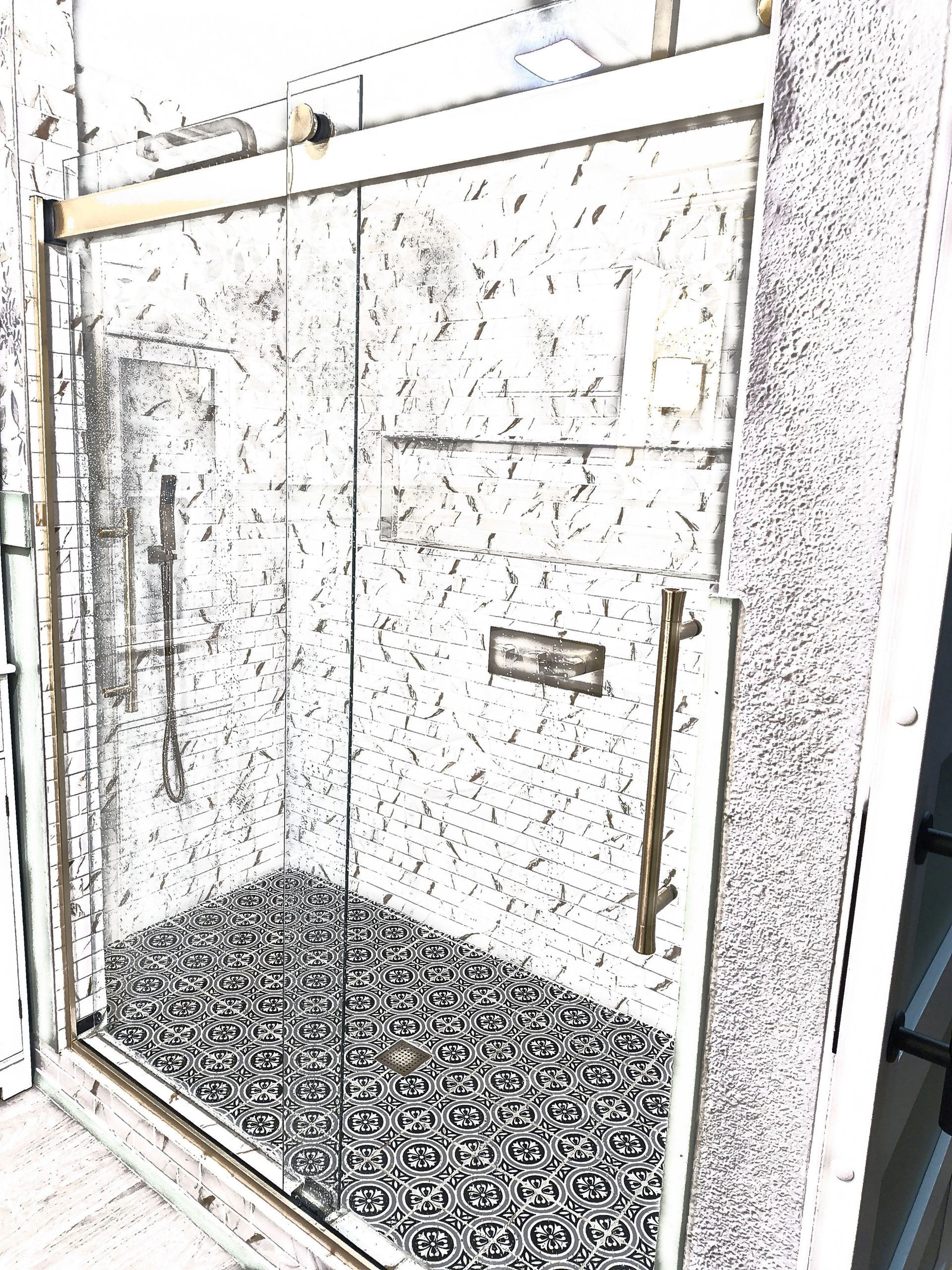 Glass shower enclosure with brass handles and a speckled tile floor in a bathroom.