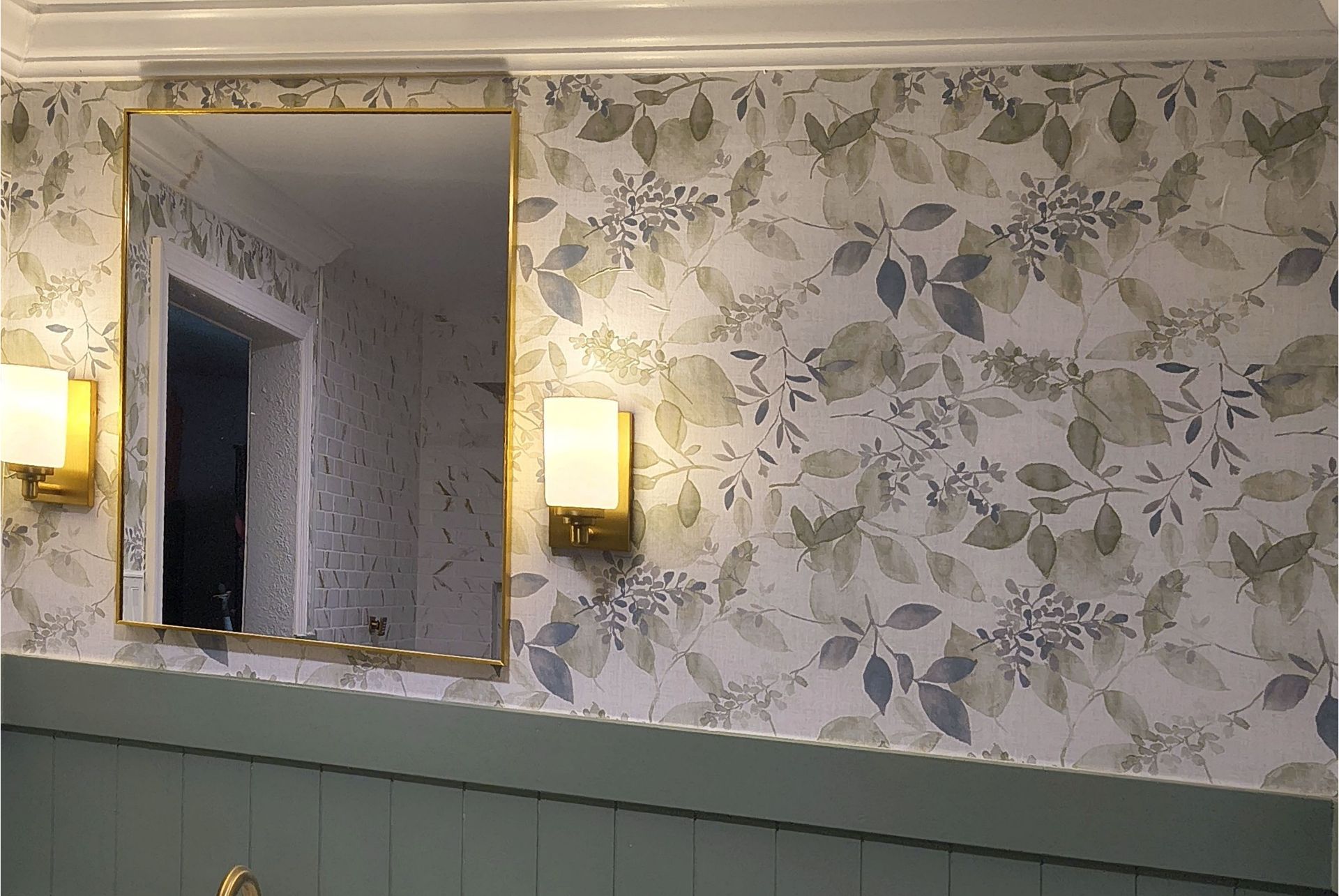 Framed mirror and wall sconces above floral wallpaper in a softly lit room