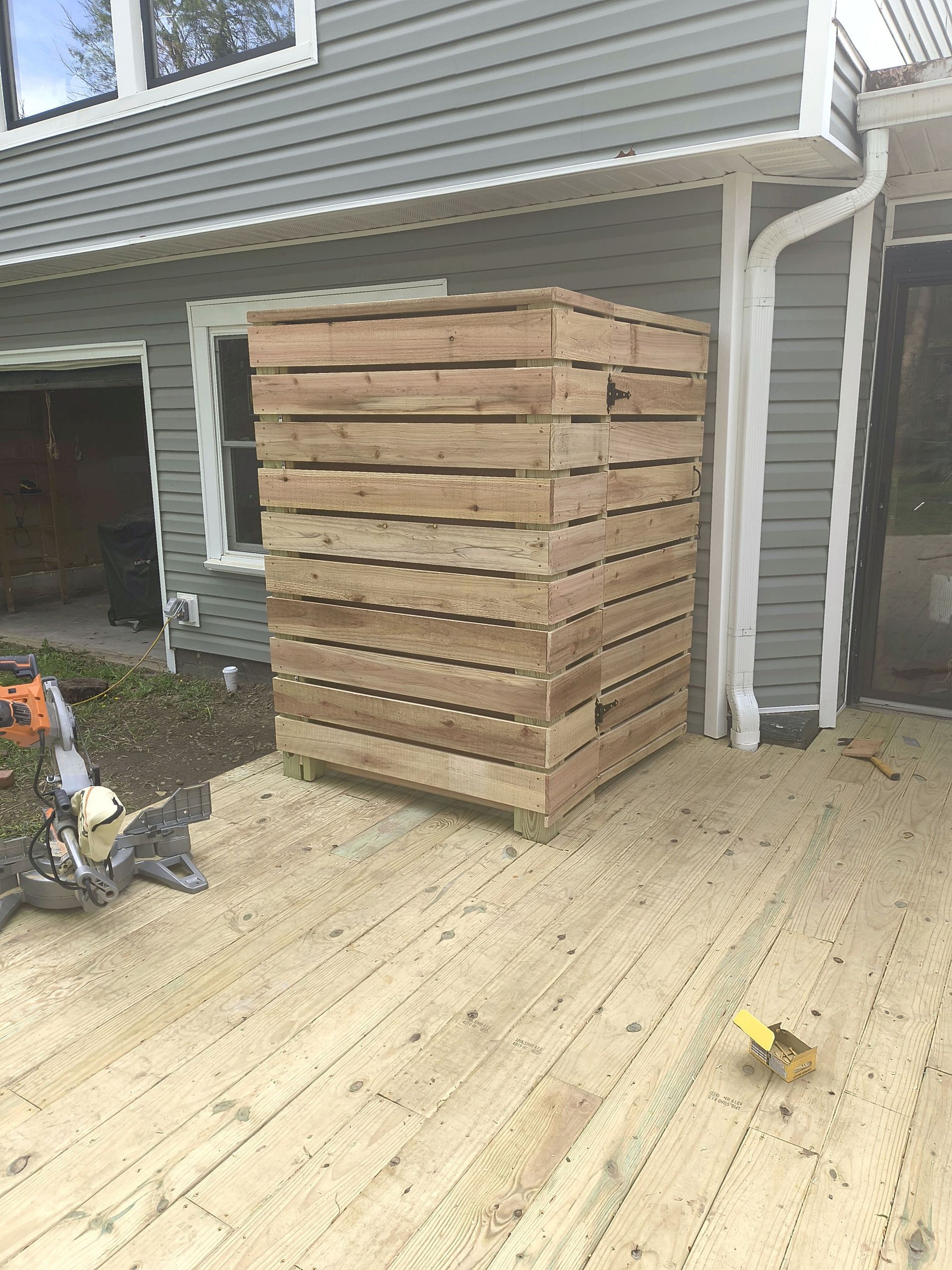 Stack of lumber on a deck beside a house with a ladder and tools nearby