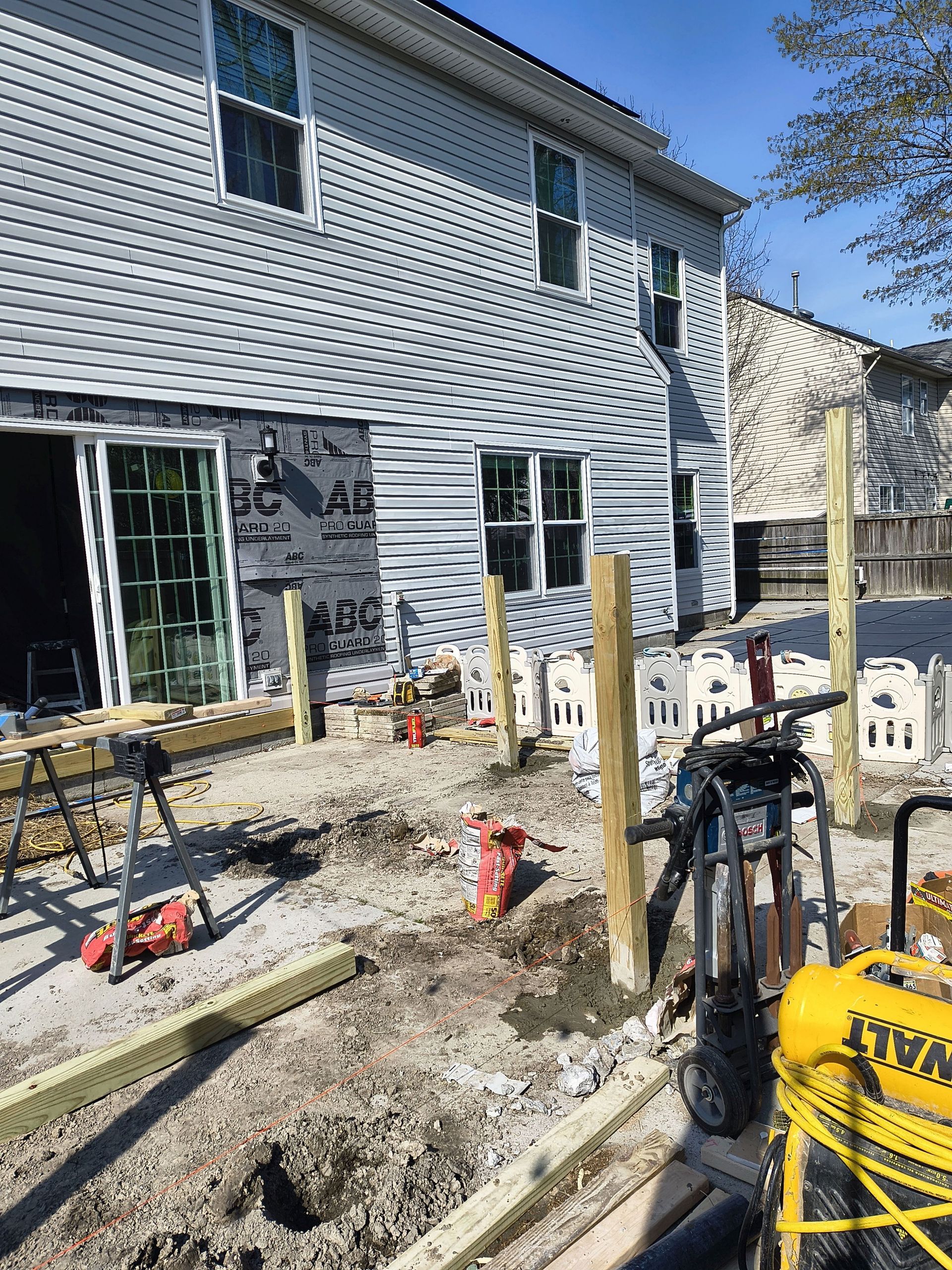 Foundation work with excavator and construction tools beside a house under renovation.