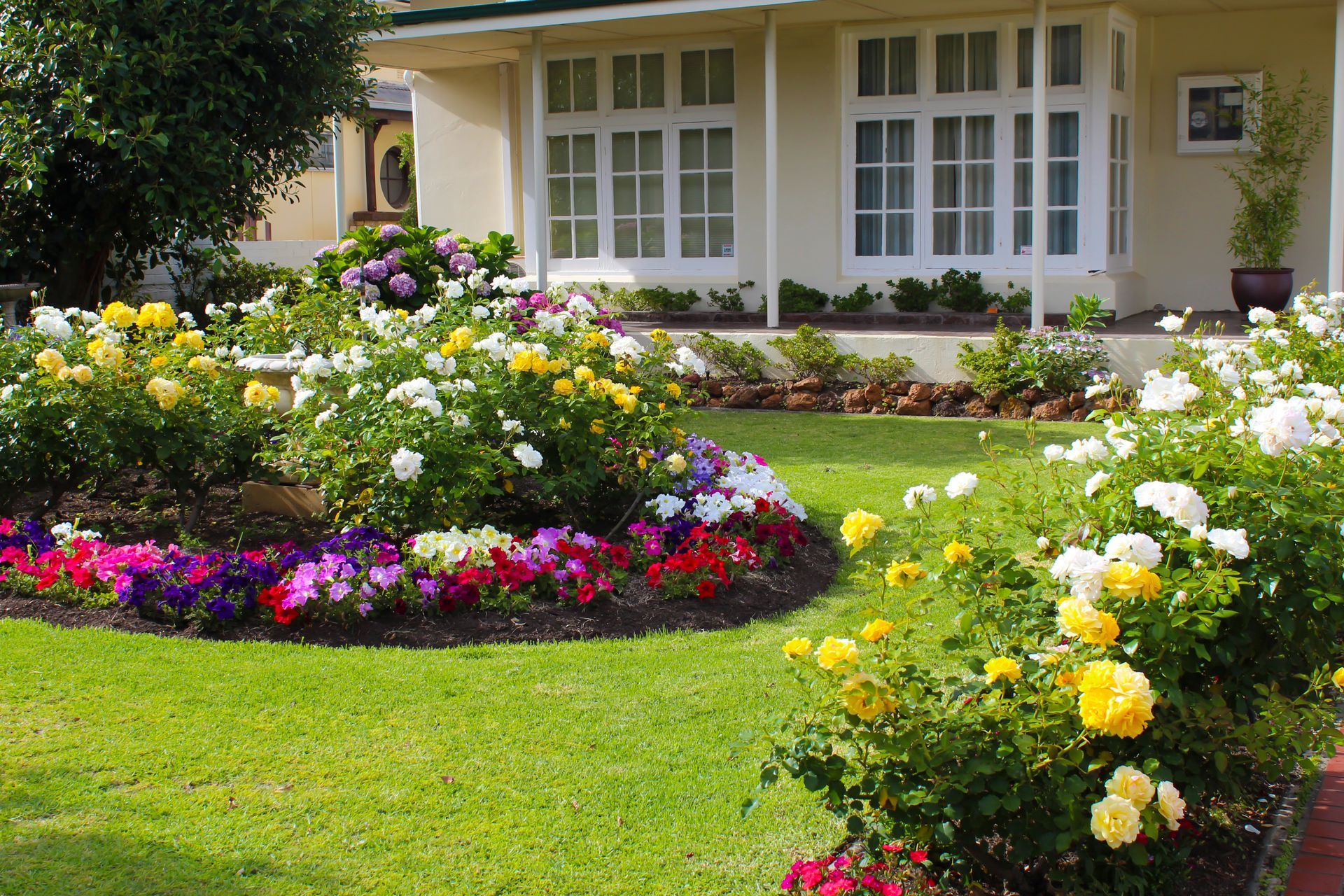 Front yard with colorful flower beds in front of a house with white windows and a porch