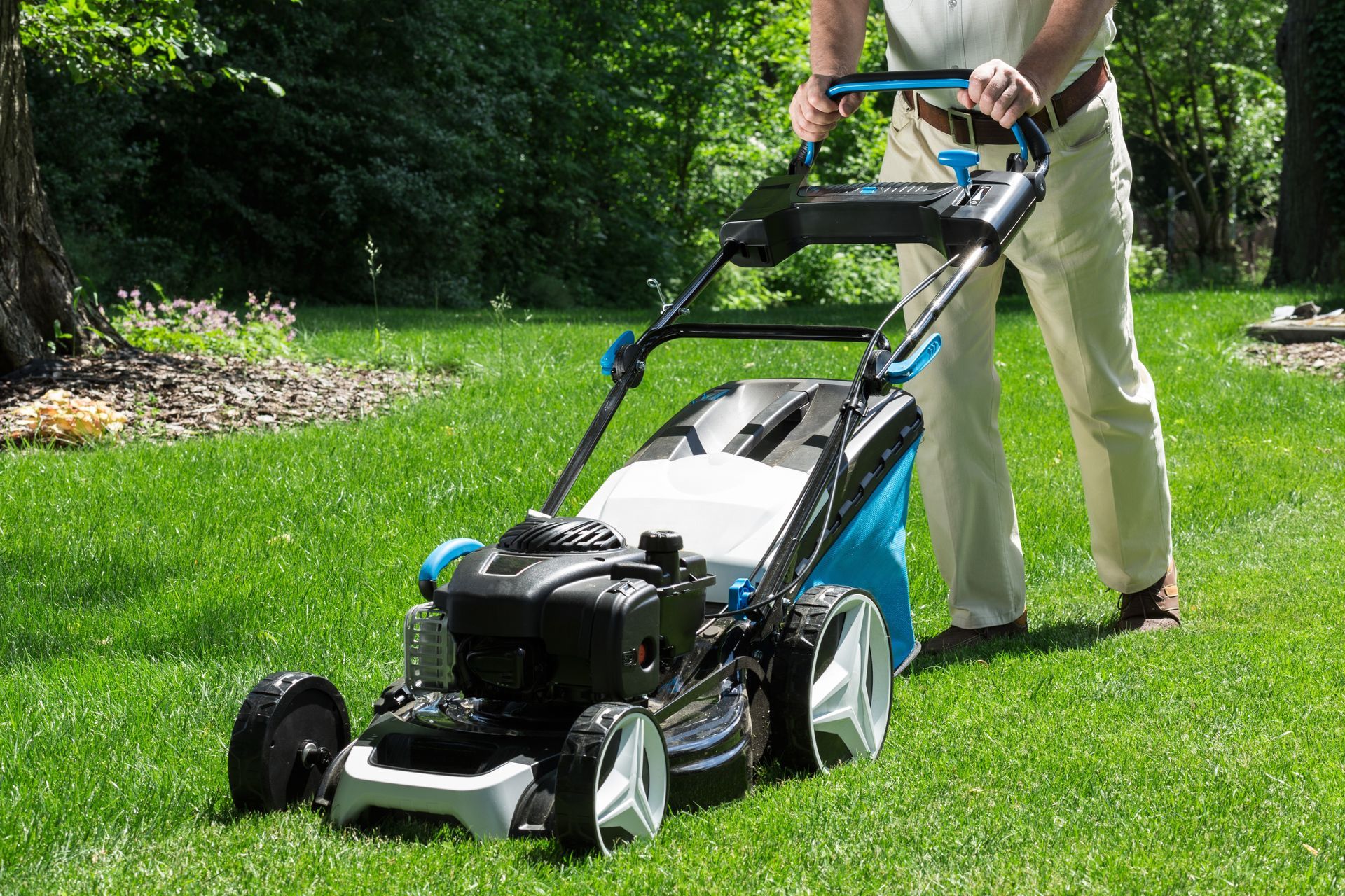 Person mowing a green lawn with a black and blue push mower in a garden.