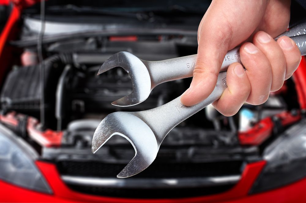 A Person Is Holding Two Wrenches In Front Of A Red Car — Auto Spares Morisset In Morisset, NSW