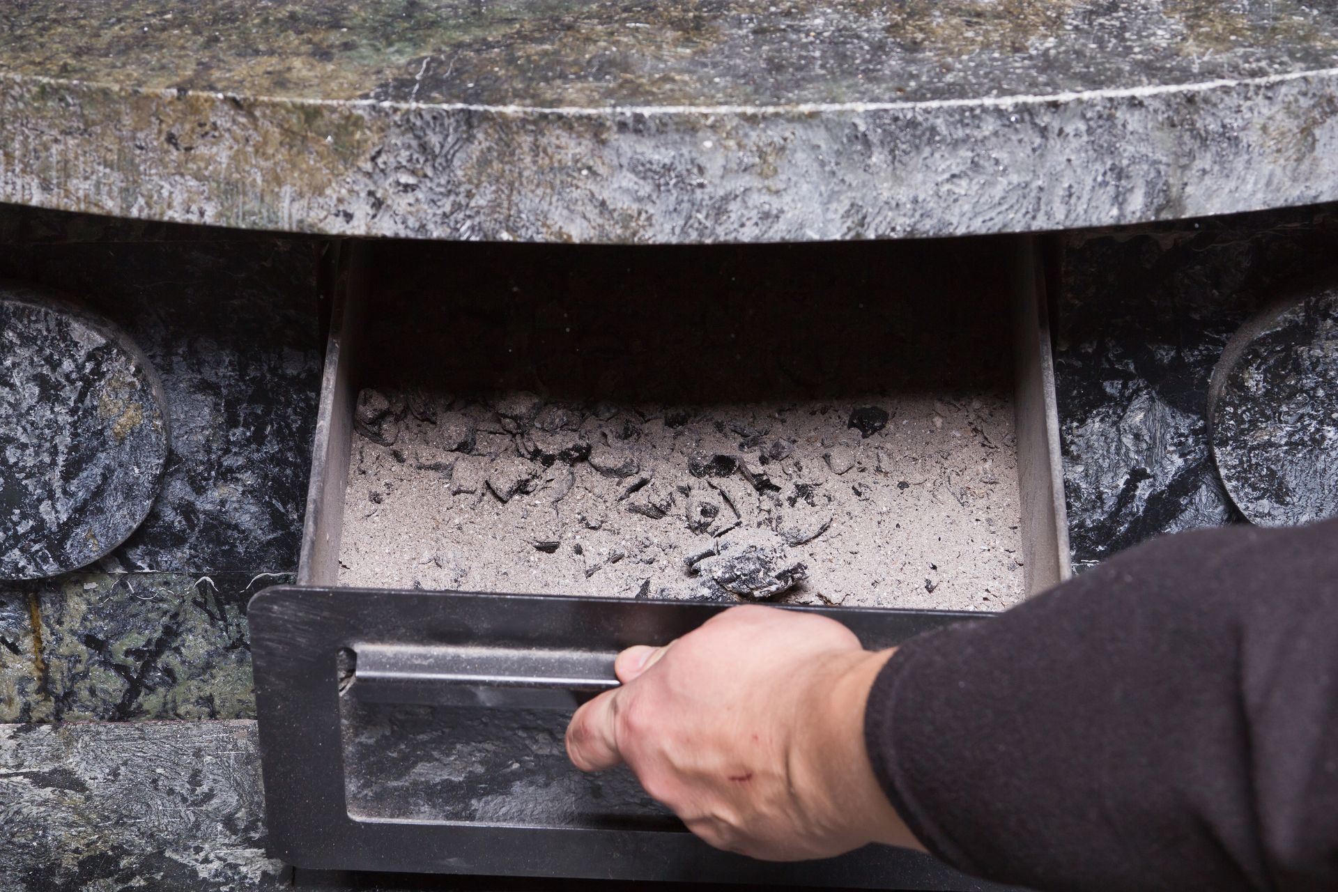 Hand placing a black tray into a stone sink with water and debris inside