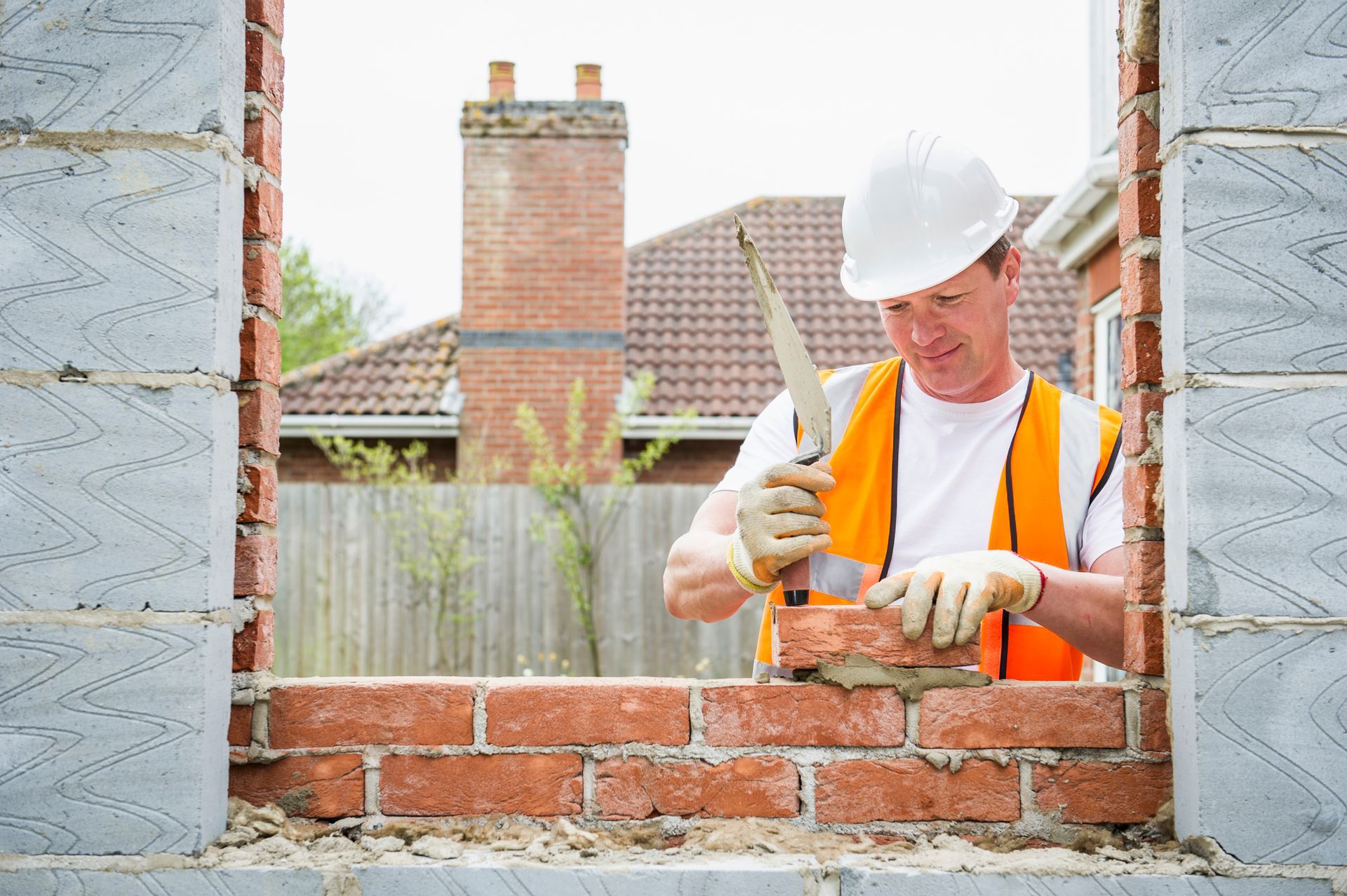 Construction worker laying bricks with mortar Construction worker laying bricks in a window opening, wearing a hard hat and safety vest.