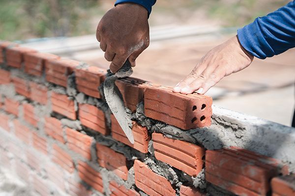Close up hand of bricklayer worker installing bricks on construction site. Hands of a bricklayer using a trowel to apply mortar on a red brick in a construction setting.