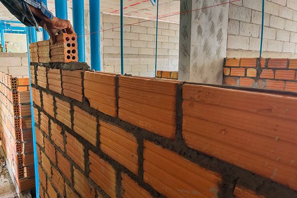 Workers help build bricks into the shape of the structure. Bricklayer laying bricks, building a wall outdoors.