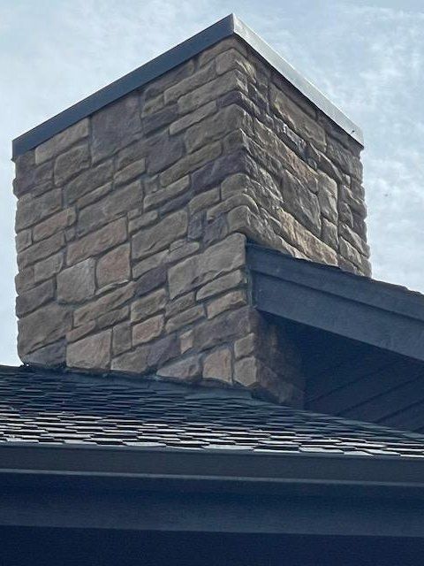 Stone chimney on a dark shingle roof with a flat black cap.