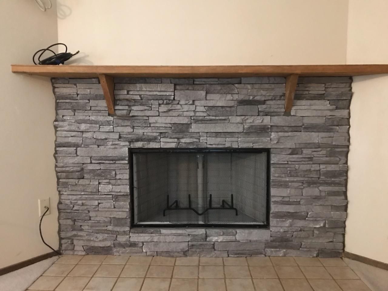 Stone-faced fireplace with black screen and wooden mantel, set against beige walls and tile floor.