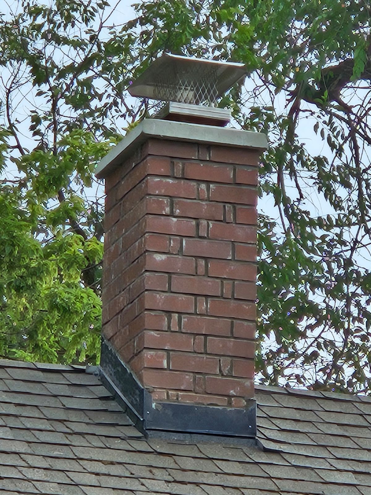 Brick chimney with a metal cap on a shingled roof.