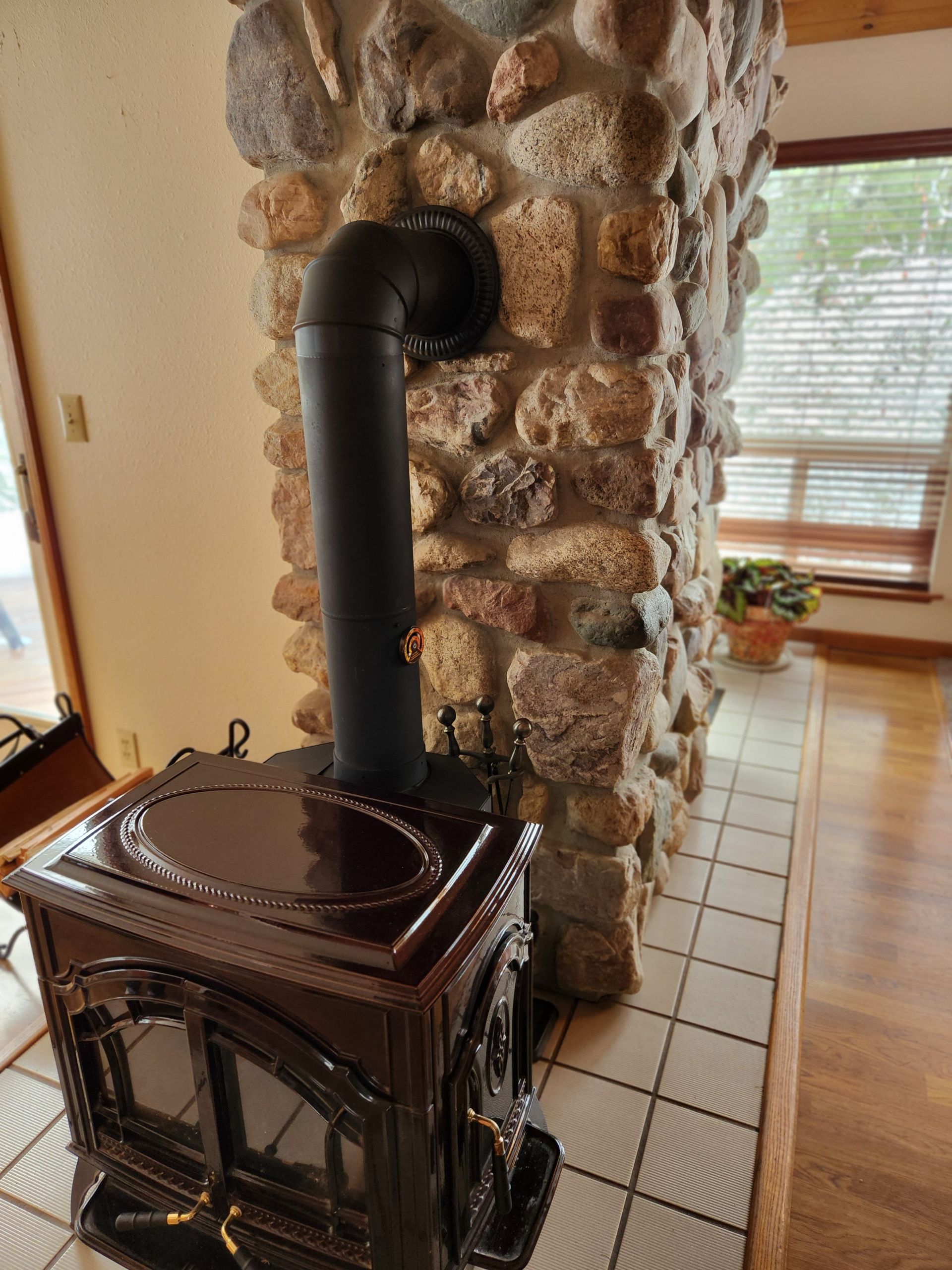 Dark wood-burning stove with black pipe against a stone chimney. White tiled hearth and wood floor.