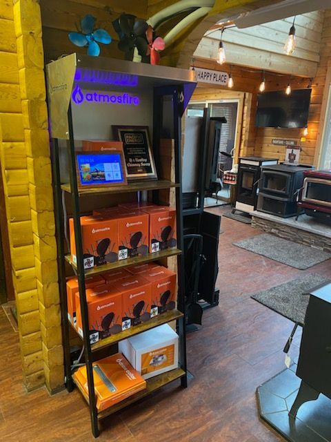 Shelving unit displaying orange boxes with product logos in a retail store with wood flooring and various stoves.