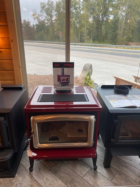 Red wood-burning stove with glass door and black top, displayed in a showroom window.