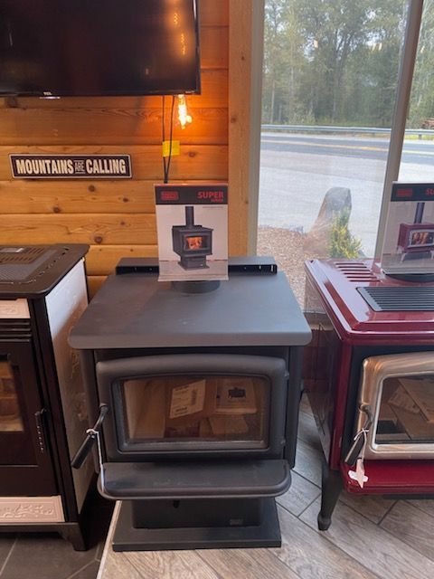 Black wood-burning stove on display in a showroom, with a sign on top.