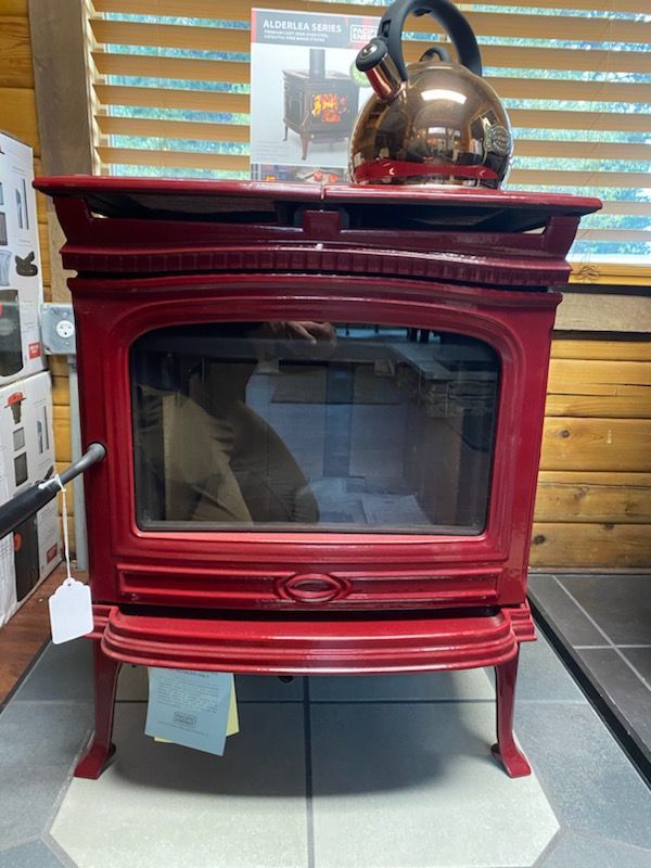 Red wood-burning stove with a copper kettle on top; indoor setting.
