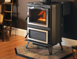 Black cast-iron stove with glowing fire in a cozy room on a rug beside wooden floors and a wall trim.