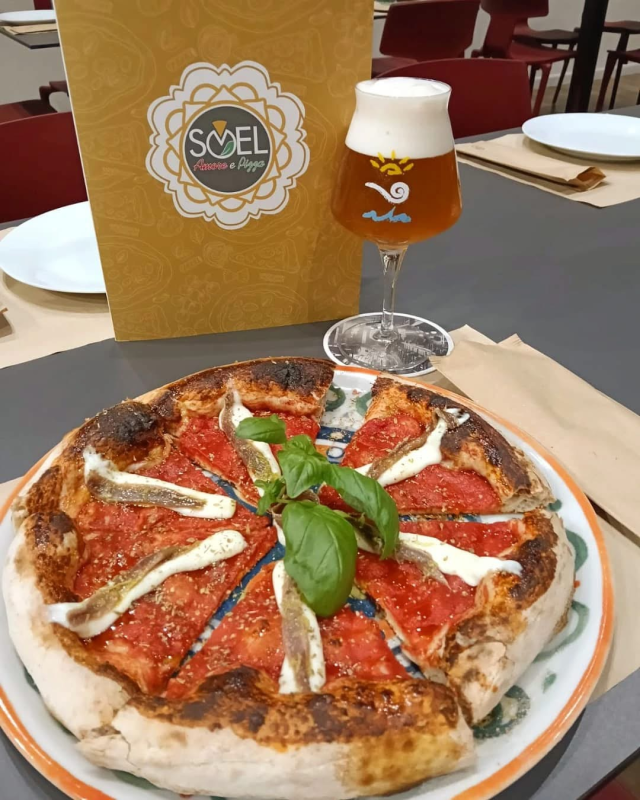 Una pizza su un piatto accanto a un bicchiere di birra
