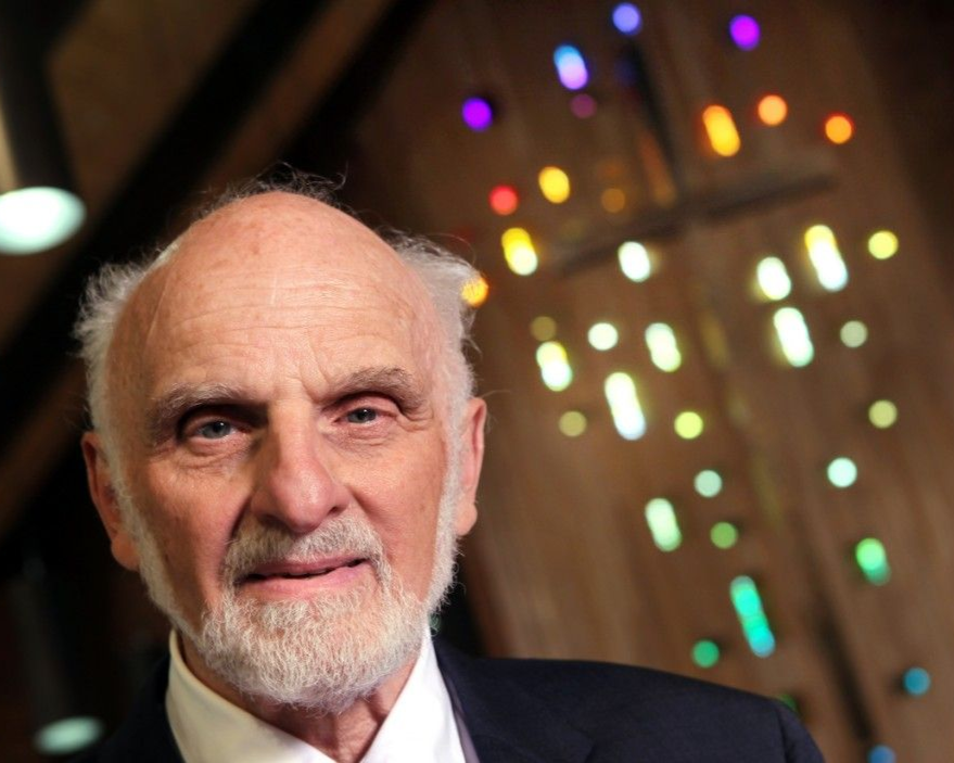 Walter Brueggeman in a suit smiling, with a colorful stained-glass window in the background.