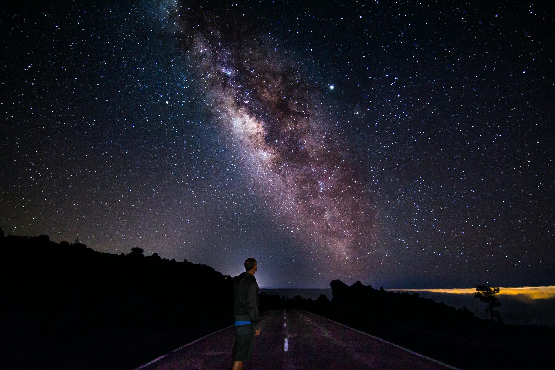 Man standing on a road gazing at the Milky Way galaxy in a dark sky.