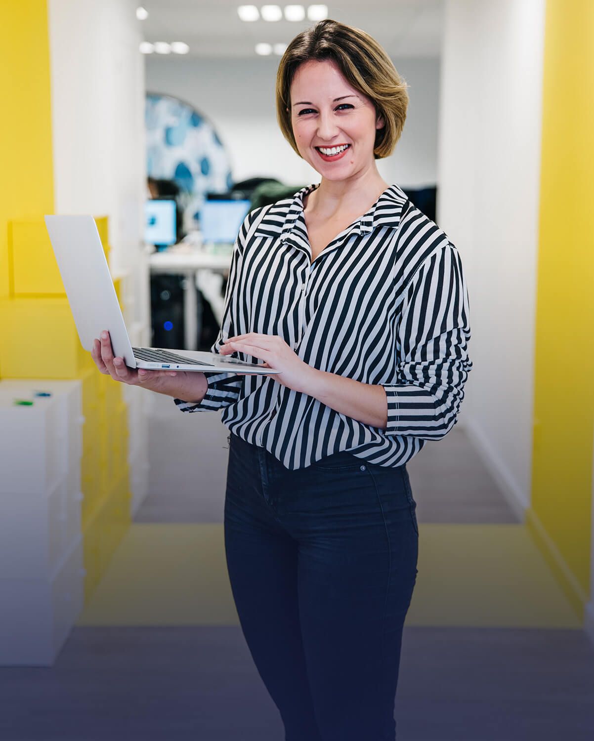 Mujer con camisa a rayas y pantalones oscuros, sonriendo, sosteniendo una computadora portátil