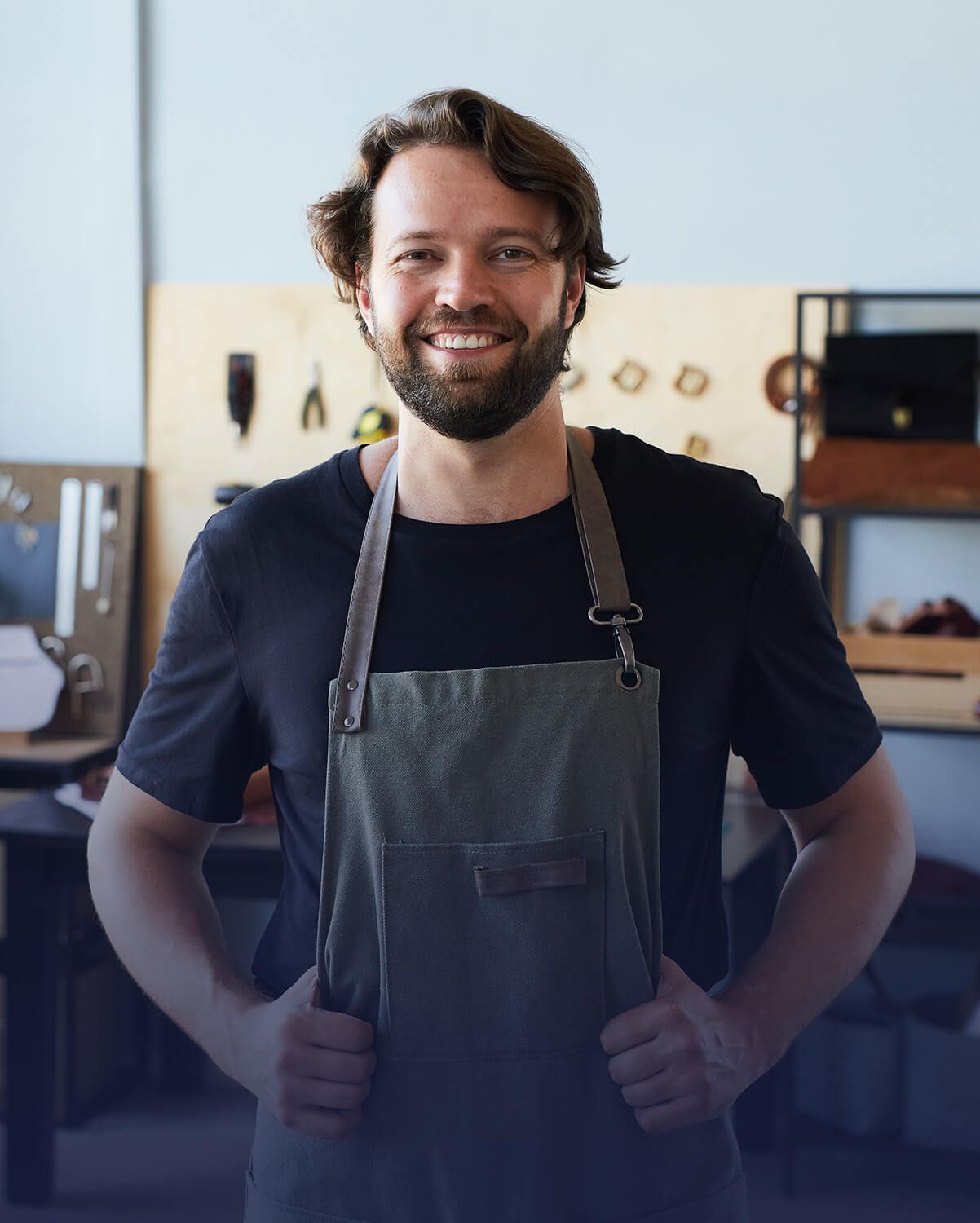 Hombre con delantal sonriendo, con las manos en las caderas, en el taller.