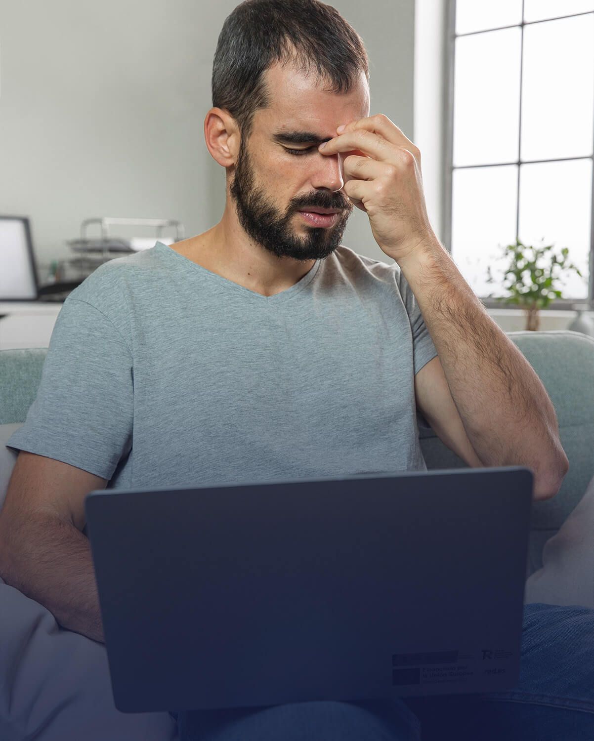 Hombre con barba sujetándose la cabeza, luciendo estresado por su Kit Digital mientras usa una computadora portátil.