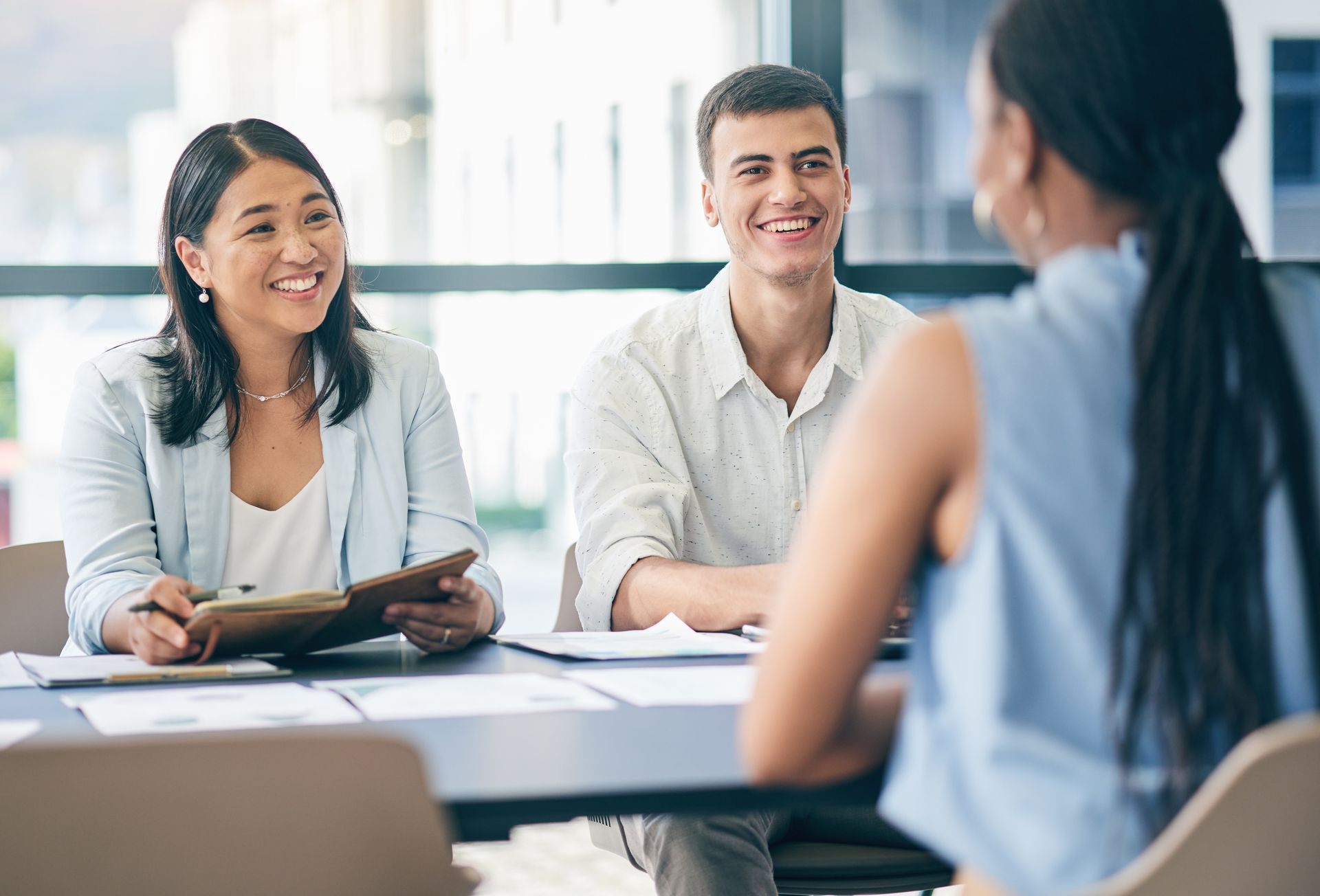 Deux intervieweurs souriants, face à une personne assise à une table dans un bureau.