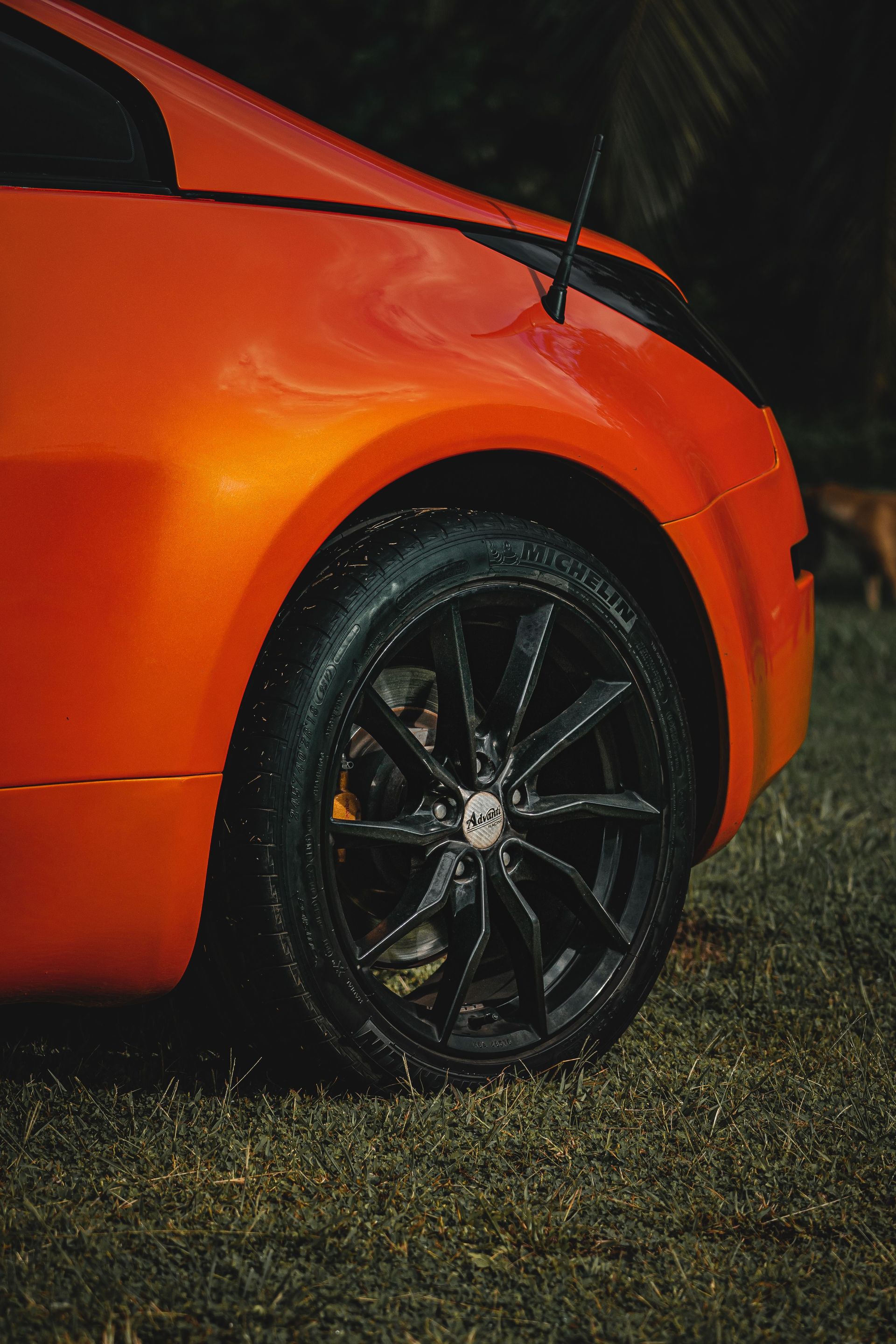 Orange sports car front wheel with black rim on wet grass at night