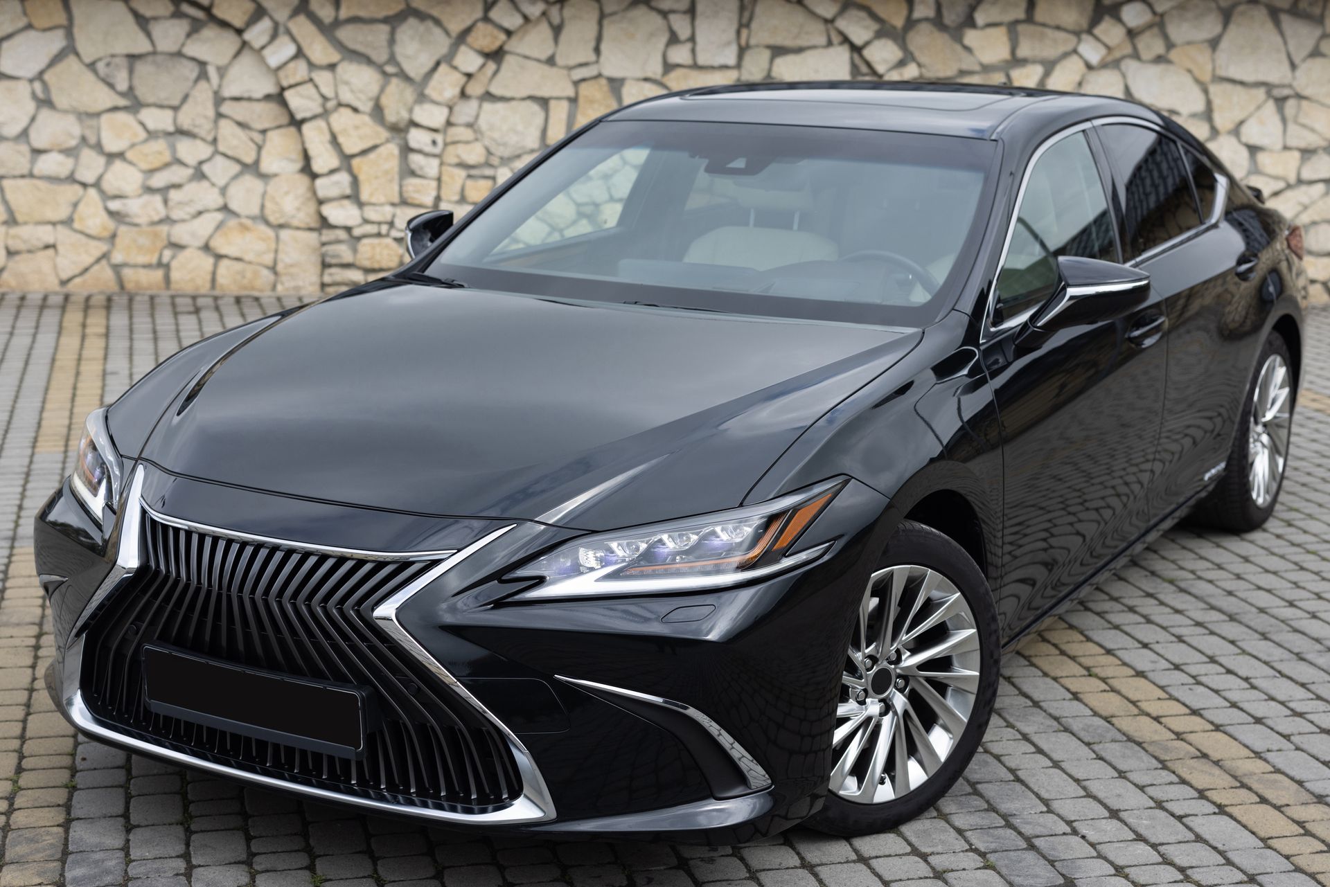 Black Lexus sedan parked on a stone-paved driveway in front of a rock wall