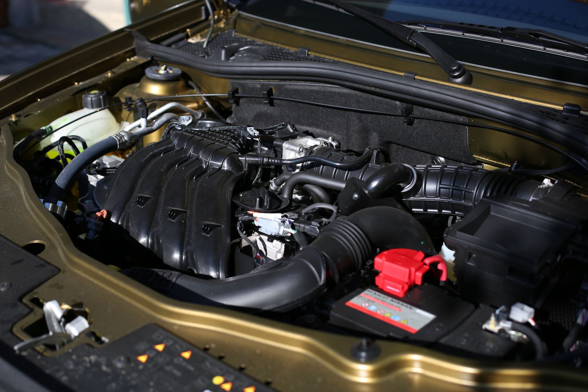 Car engine bay with black intake manifold and a red battery terminal cover