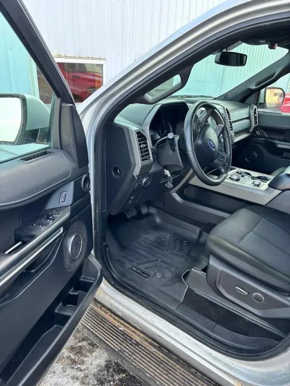 Open car door showing damaged interior, torn steering wheel, and debris on the floor.
