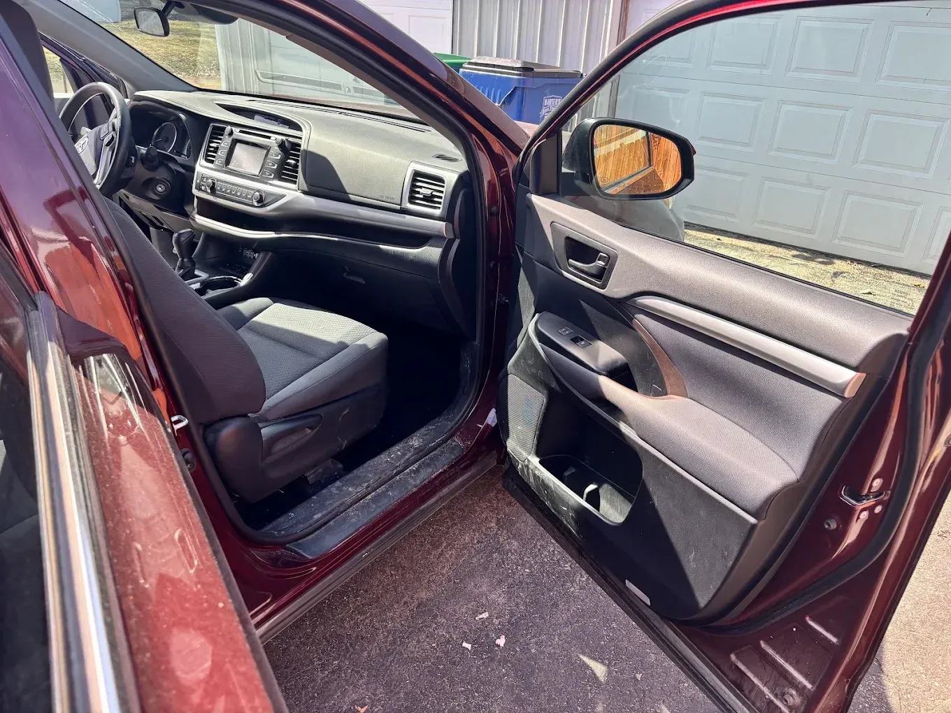 Open car door showing a maroon sedan’s gray interior and dashboard.