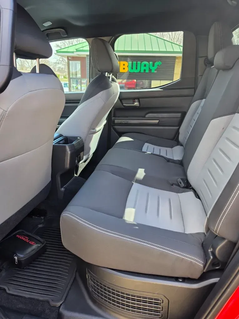 Car interior with gray rear bench seats and black floor mats, viewed from the open rear door.