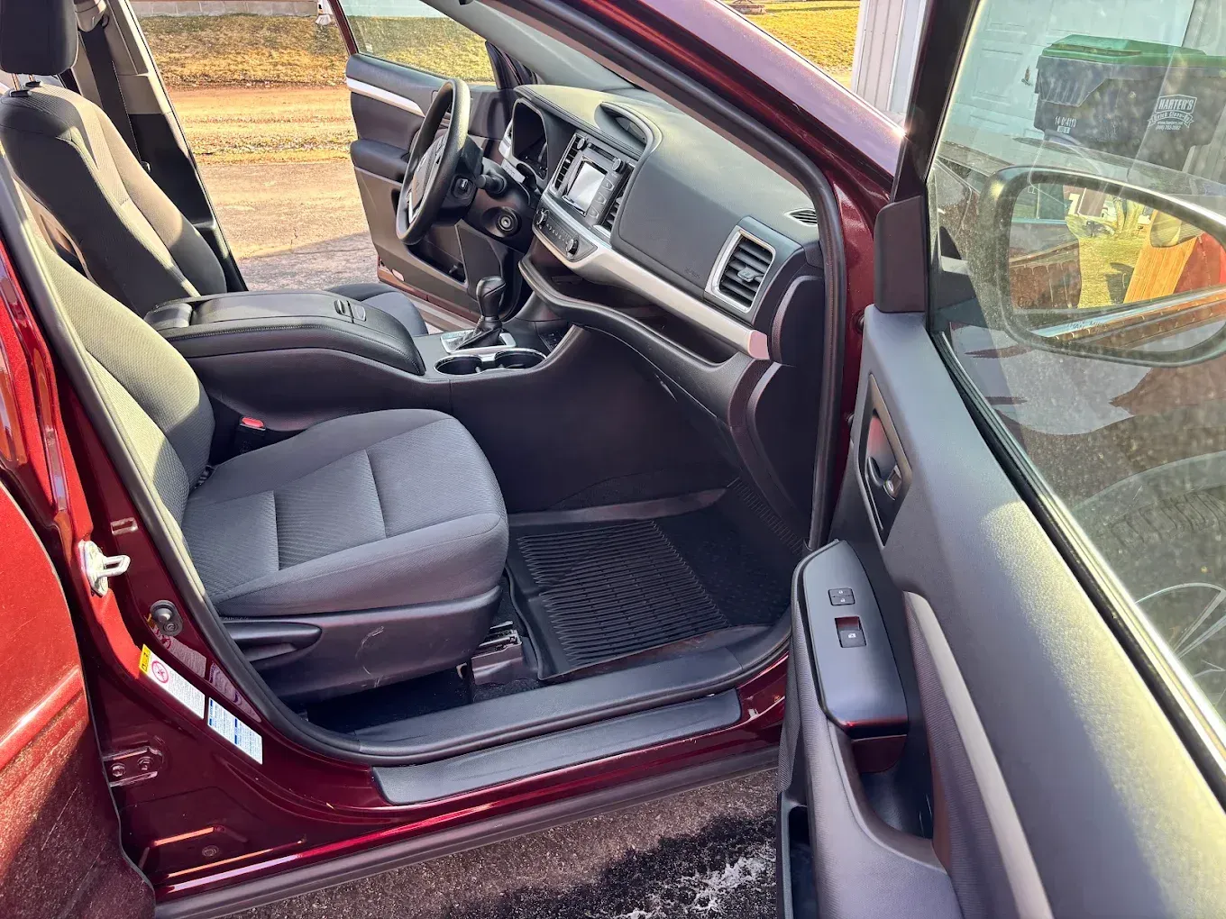 Open driver-side door showing a gray car interior with seats, dashboard, and center console.