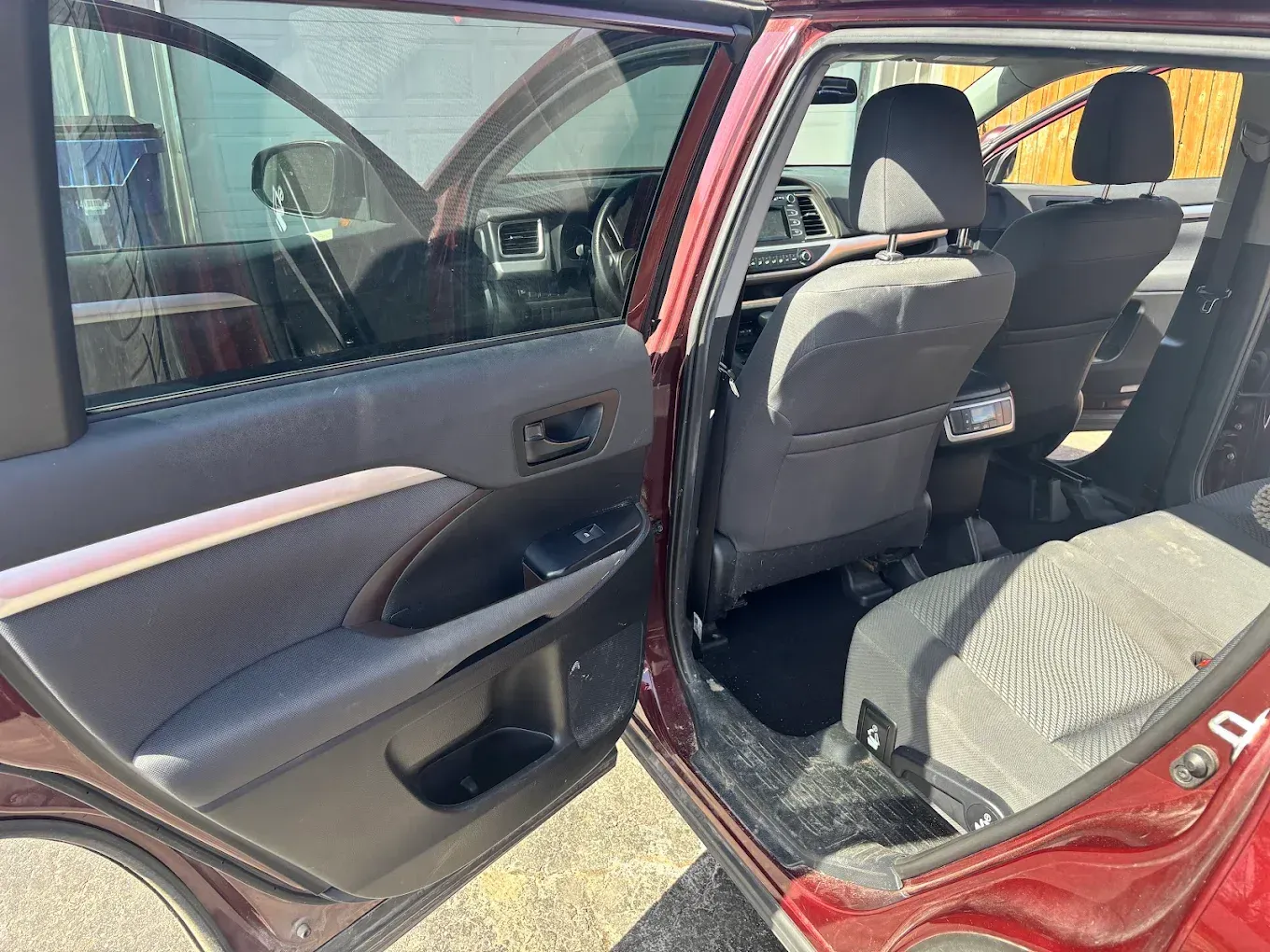 Open car rear door showing black interior seats and red exterior in daylight