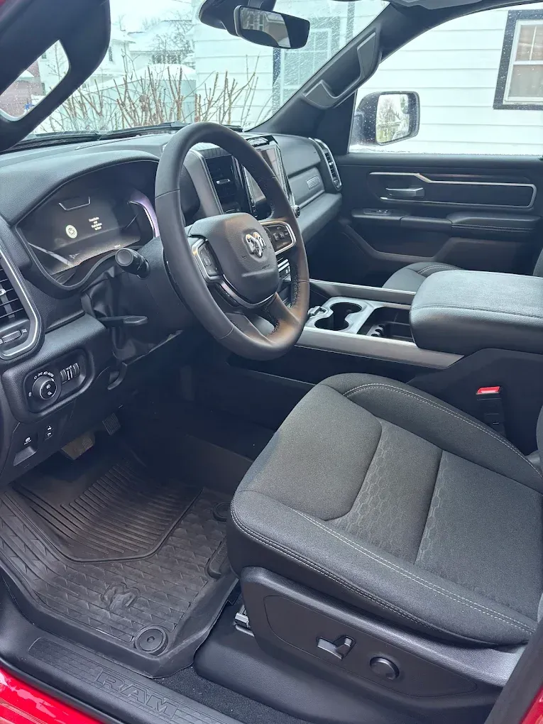 Truck cab interior with steering wheel, black seats, and center console viewed from the open driver’s door