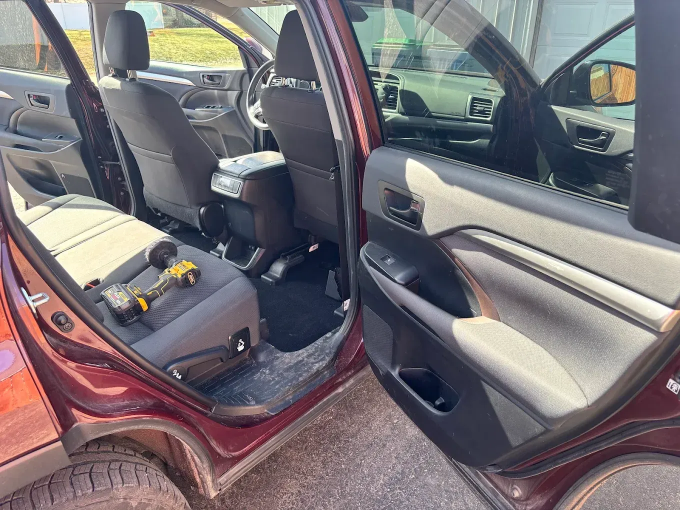 Open car rear door showing gray seats and a yellow tool on the back seat