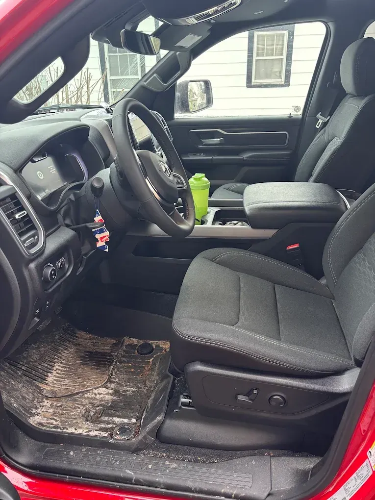 Black truck interior with driver seat, steering wheel, and worn floor mat, viewed from open door