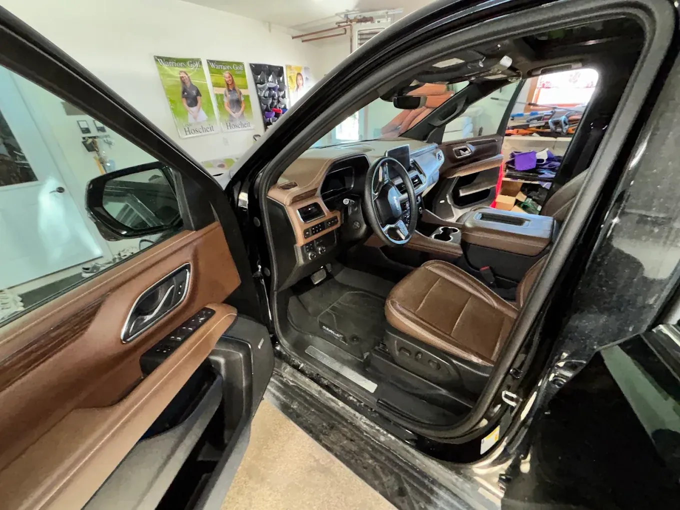 Open driver’s door of a black car, showing a tan leather interior and dashboard.