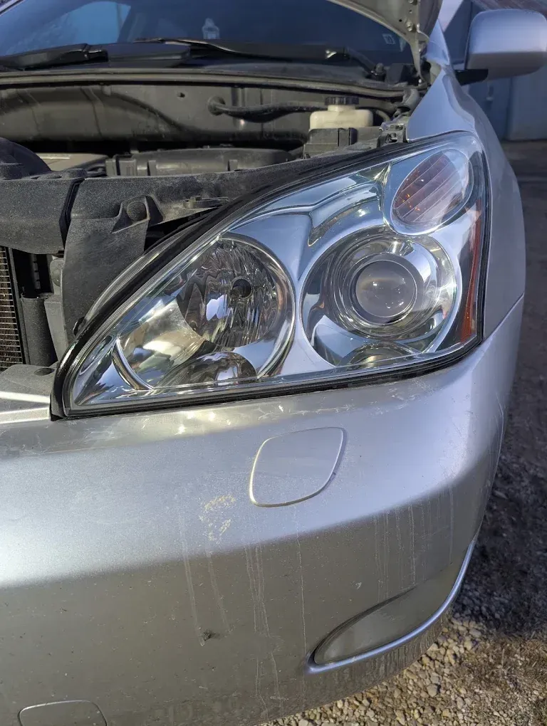 Close-up of a silver car’s front-right headlight and fender with the hood open, showing front-end damage.