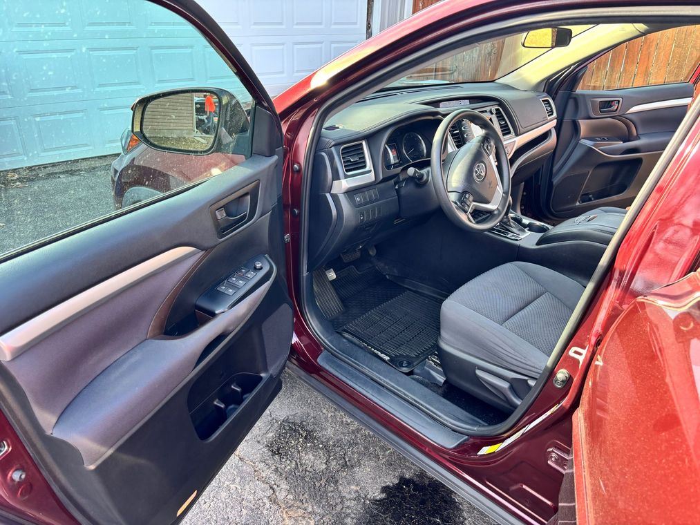Open red car door showing black interior and driver’s seat near a brick wall.