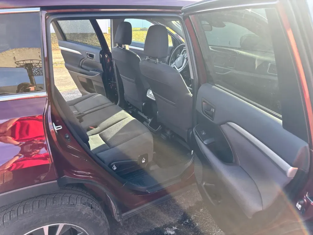 Open rear door of a maroon car, showing the gray back seat interior.