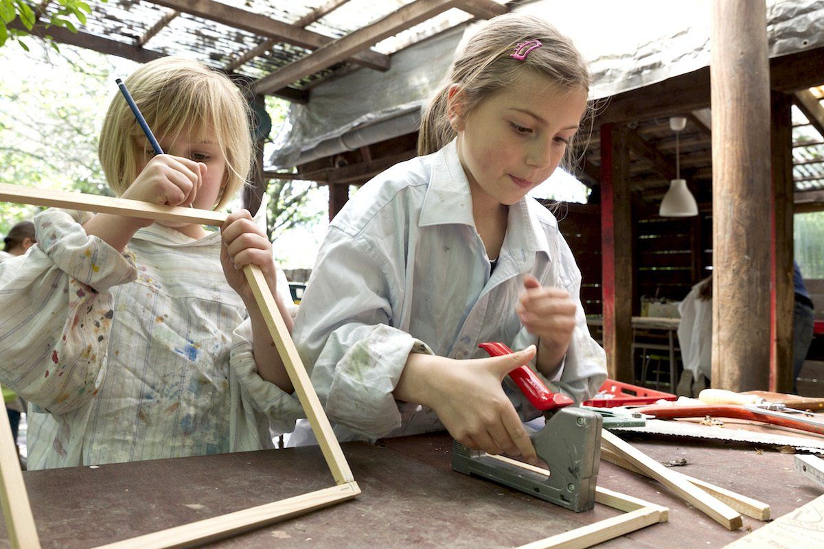 Zwei Kinder arbeiten im Freien mit Holz und Werkzeugen.