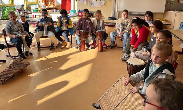 Kinder sitzen im Kreis und spielen in einem Klassenzimmer Perkussionsinstrumente.
