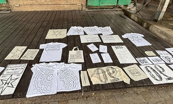 Weiße bedruckte T-Shirts und Schilder lagen auf einer Holzterrasse, viele davon mit Stern- und Wortmotiven.