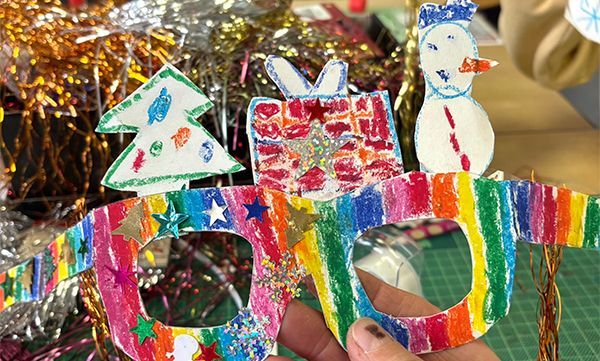 Bunte Weihnachtsgläser aus Papier mit Baum-, Geschenk- und Schneemannverzierungen. Lametta im Hintergrund.
