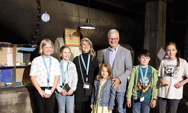 Gruppenfoto mit Erwachsenen in industrieller Umgebung, lächelnd, mit Namensschildern.