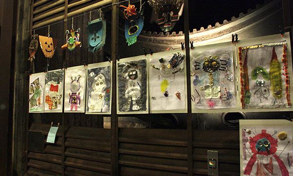 Kunstwerke sind an einer Wand ausgestellt. Bunte Zeichnungen und Masken hängen vor einem Holzhintergrund.