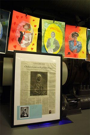 Ausstellung von Kunstwerken und Zeitungsausschnitten; Porträts, herzförmige Hintergründe und ein gerahmter Zeitungsartikel.